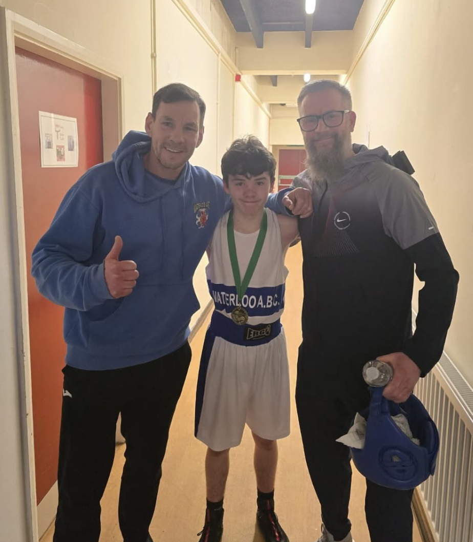 Young boxer with medal flanked by two proud coaches at Waterloo ABC